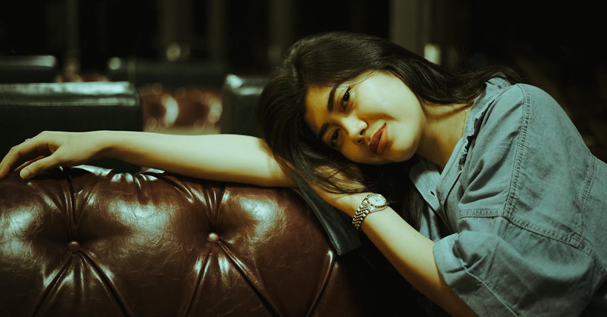 A serene woman in casual attire rests on a luxurious leather sofa in a dimly lit room.