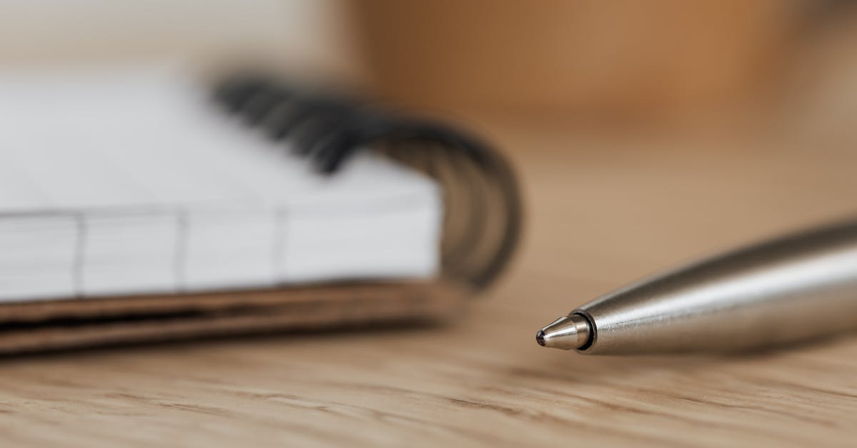 Side view closeup of opened ring bound notebook with blank pages near silver ball point pen placed on wooden table