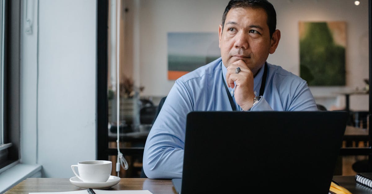 Concentrated ethnic adult male entrepreneur thinking on project while working at table with netbook and cup of drink