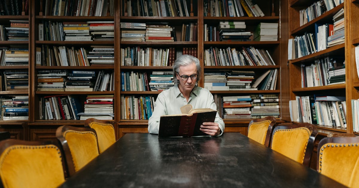 Senior man enjoying a book in a classic library with wooden bookshelves and a long table.