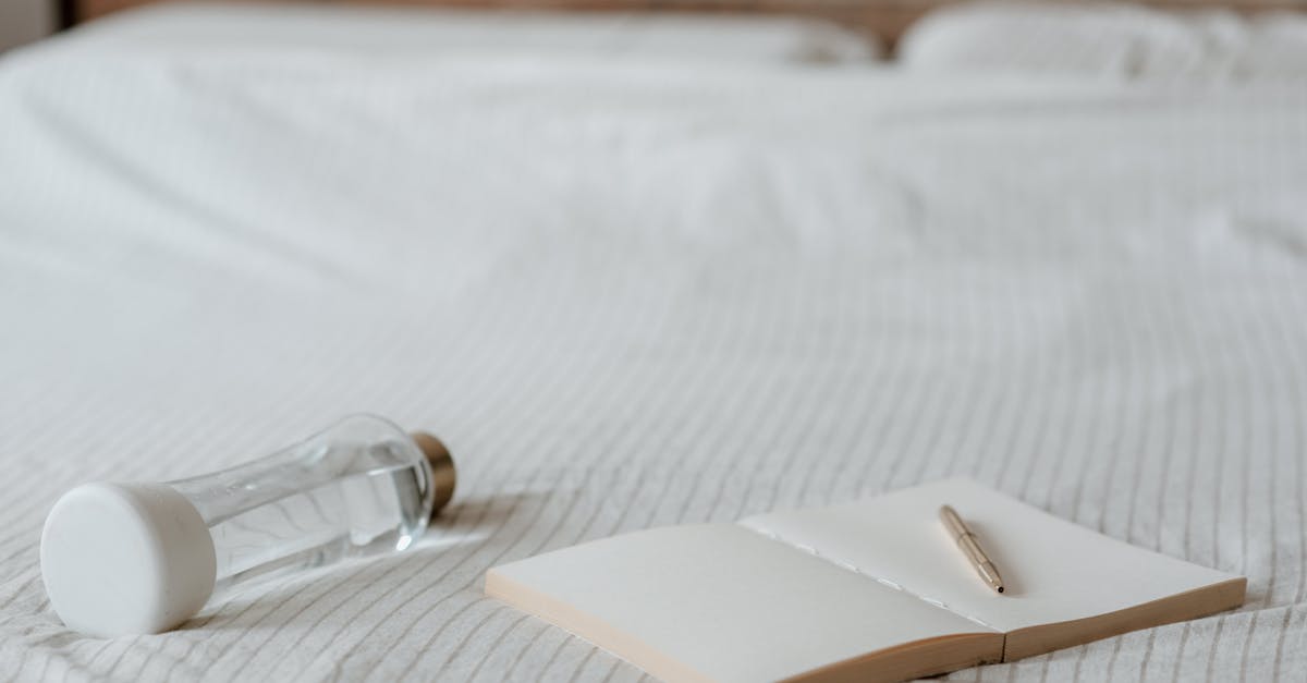 Empty diary with pen near decorative bottle of water on crumpled bed sheet at home