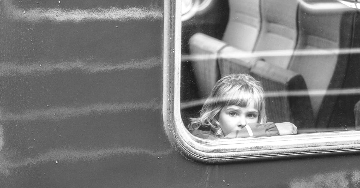 A child peeks through a train window, embodying curiosity and travel in this black and white photo.