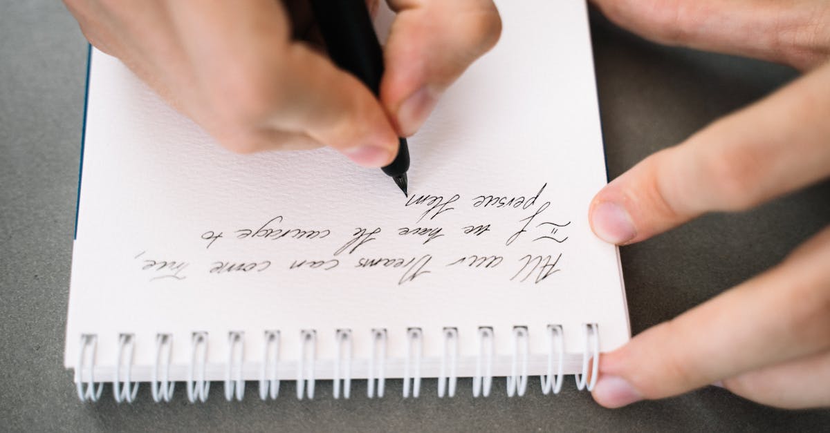 Hand holding a pen writing cursive in a notebook with elegant handwriting.
