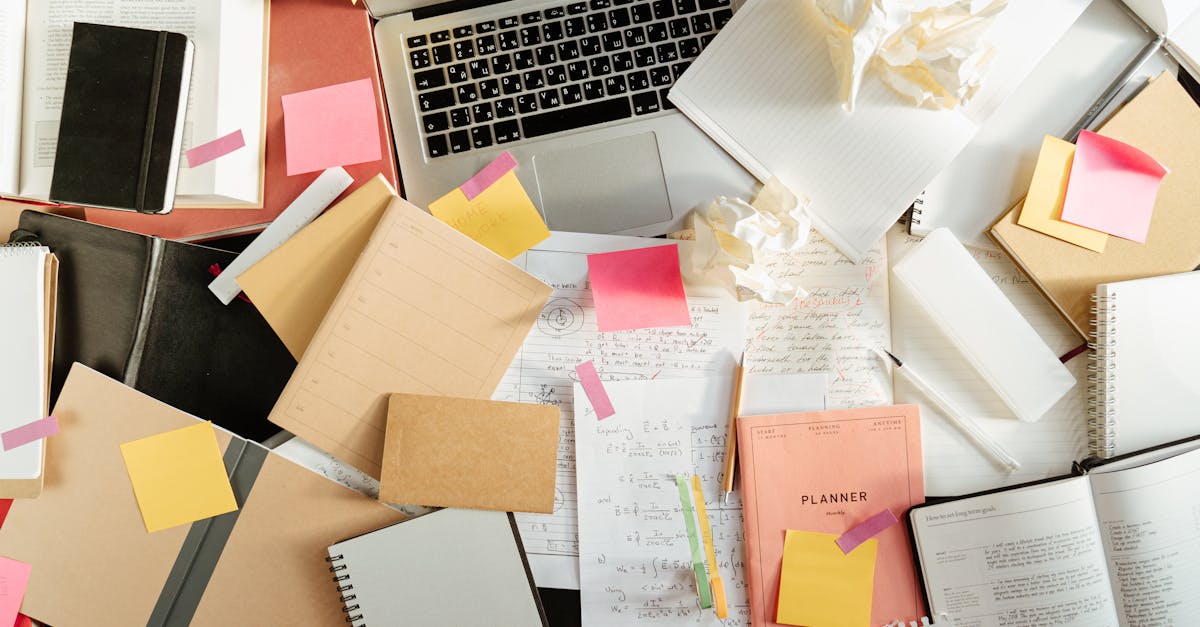 Flatlay of a messy study desk with laptop, notebooks, and sticky notes, showcasing the creative process.