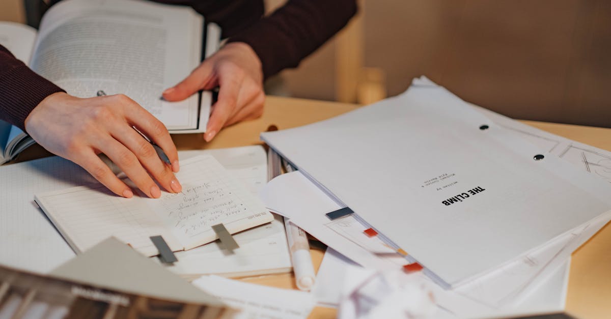 Schreibtisch mit Notizbuch, Unterlagen und offenen Büchern.