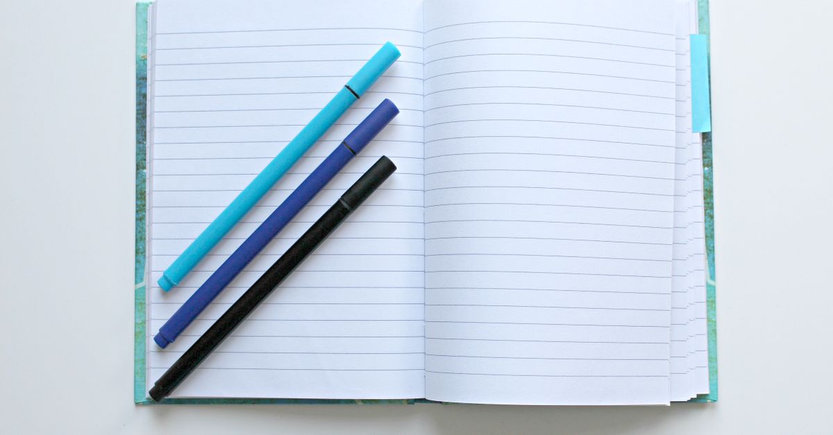 Open lined notebook with colorful pens on a white surface, perfect for note-taking and office tasks.