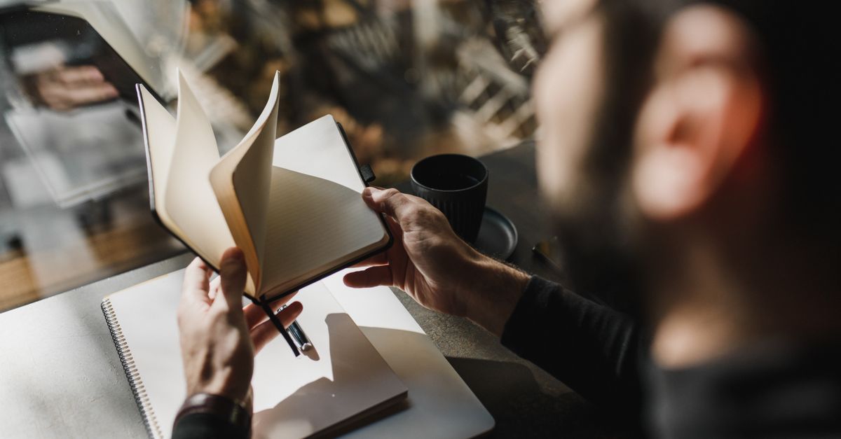 A person flips through a notebook while seated by a window, enjoying a cozy ambiance.