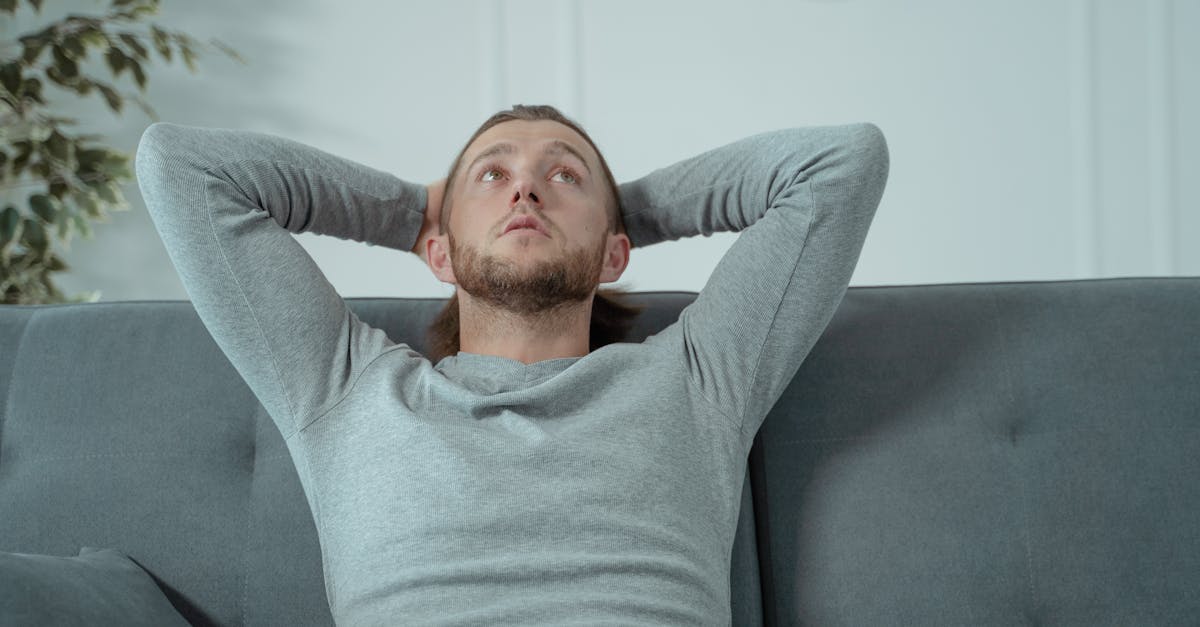Man looking thoughtful while relaxing on a grey sofa indoors, conveying a sense of contemplation and relaxatio