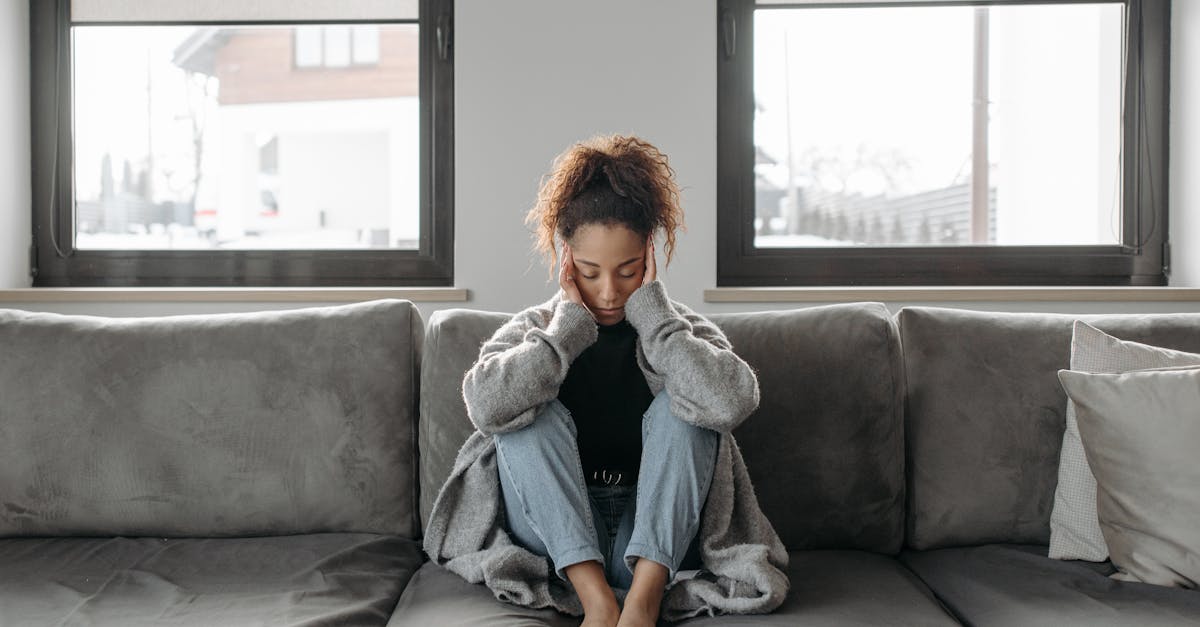 A woman sits on a sofa looking unwell, emphasizing a sense of illness or fatigue indoors.