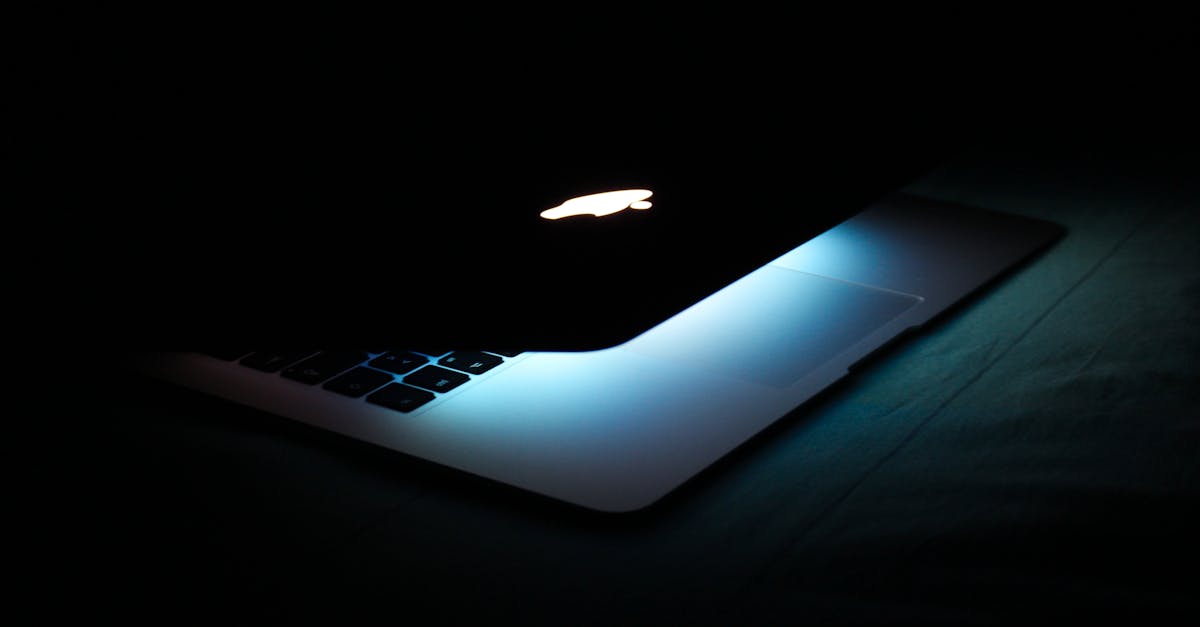 A partially closed laptop with a glowing logo and illuminated keys in a dark setting.