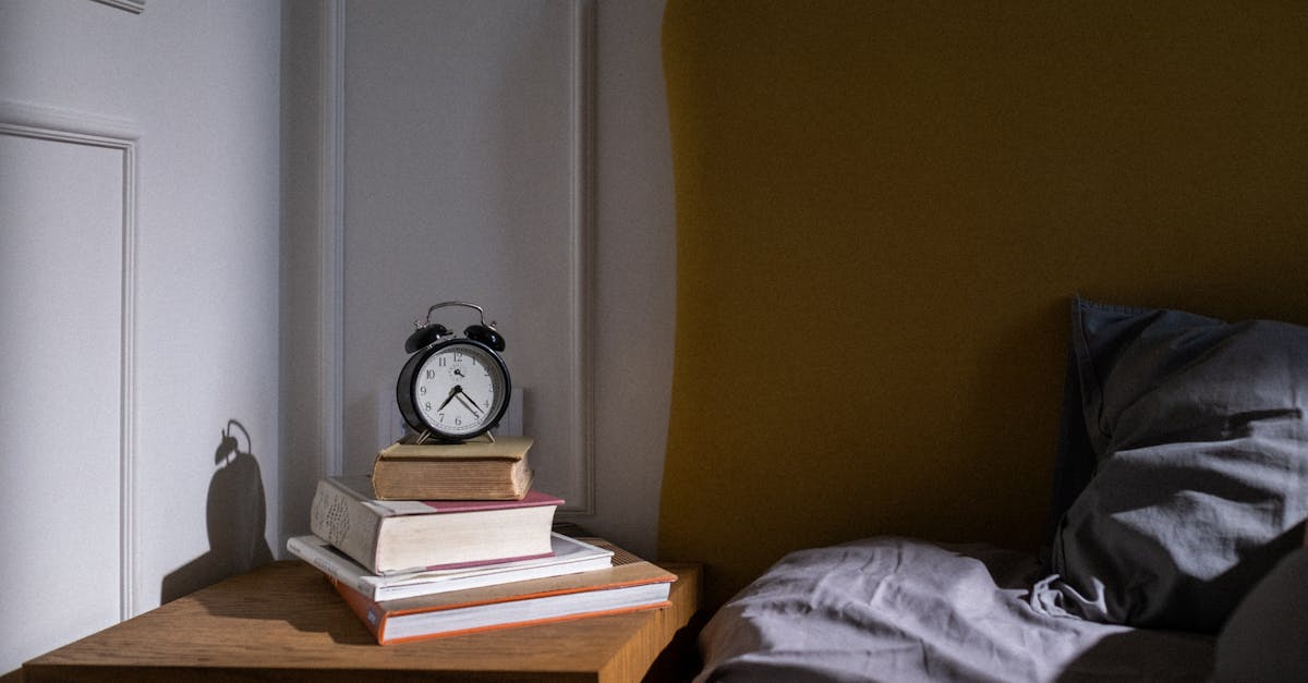 A cozy bedroom setting with books and an alarm clock on a nightstand next to a bed.