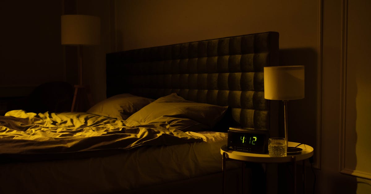 Relaxing dimly lit bedroom with an unmade bed, digital clock displaying 4:12, and warm ambient lighting.