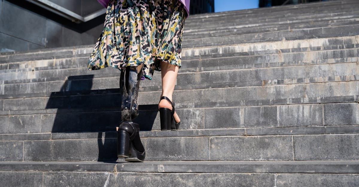Stylish woman with prosthetic leg in high heels walking up stairs outdoors in bright daylight.