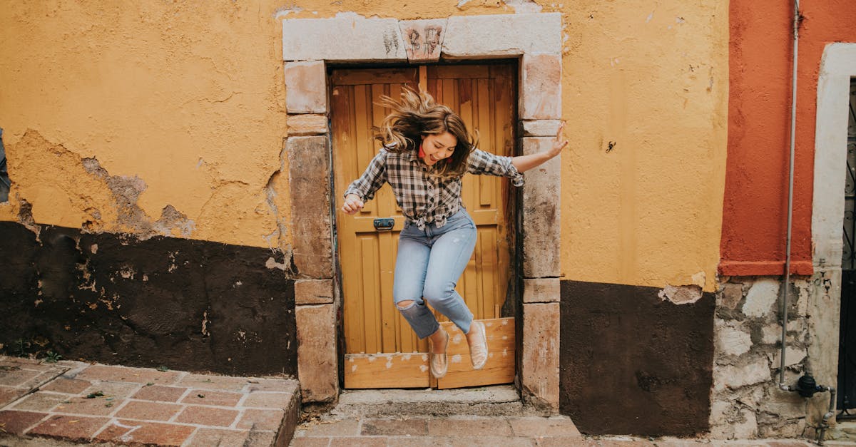 Energetic woman in casual attire leaps in front of a colorful doorway, exuding happiness and freedom.