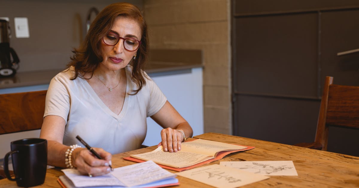 Adult woman writing notes in a cozy kitchen setting with books and a cup of coffee.