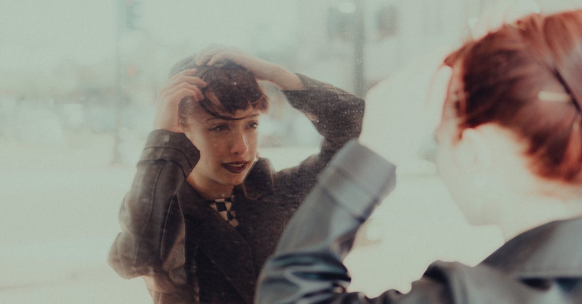 A woman adjusting her hair in a mirror, reflected with a soft and moody ambiance.