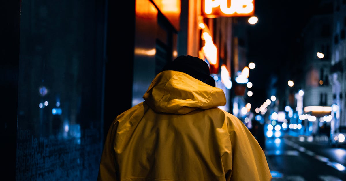 A person in a yellow jacket walks along a city street illuminated by neon pub lights at night.