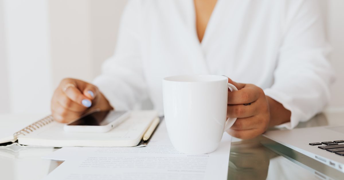 Woman holding a white mug at a desk with documents and laptop in an office.