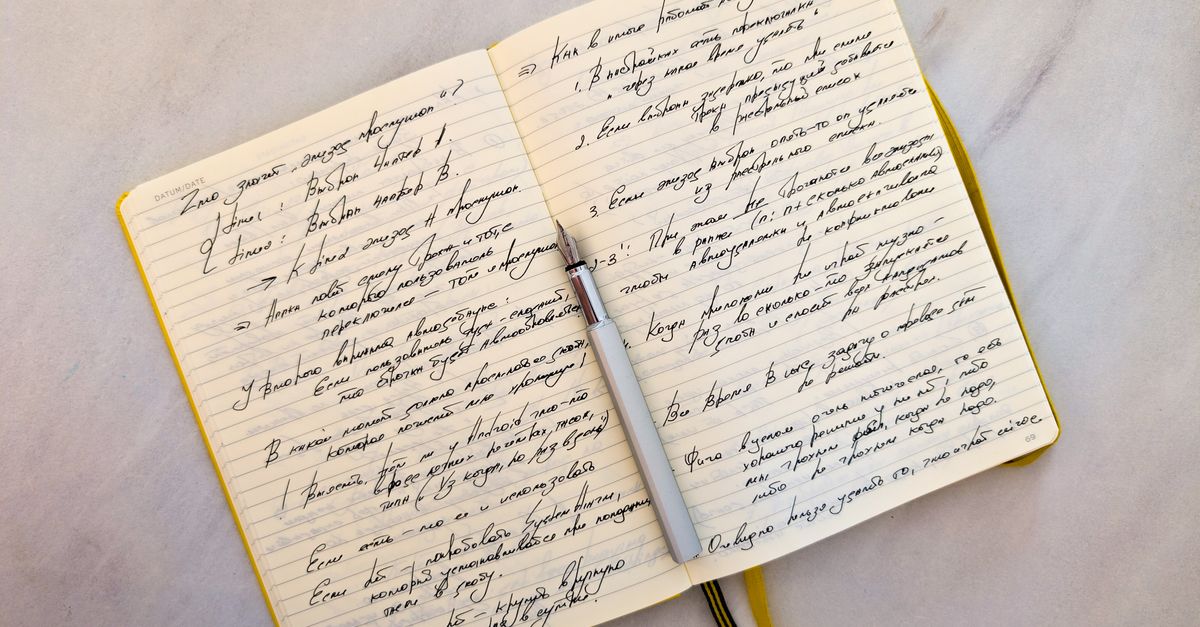 Open notebook with cursive handwritten notes on marble surface and a pen resting on pages.