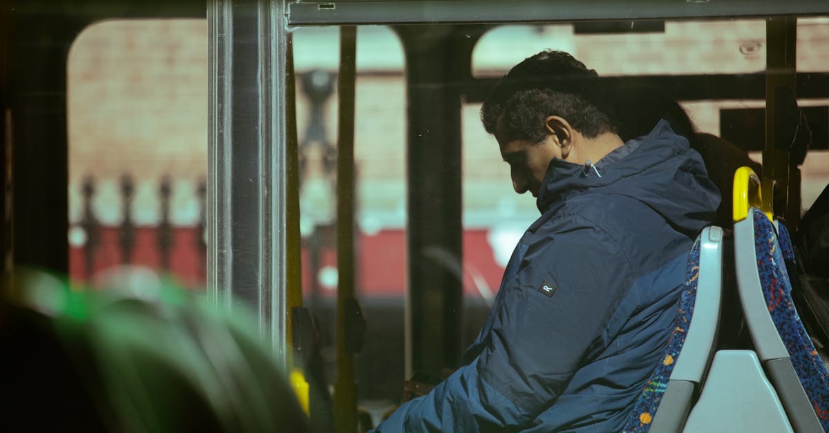 A person in a blue jacket seated inside a city bus during daytime commute.