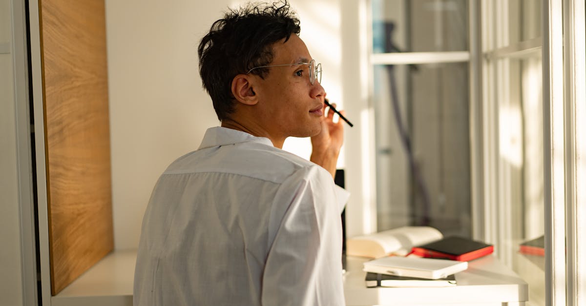 Man in white shirt gazing out window pensively, surrounded by books in modern office.