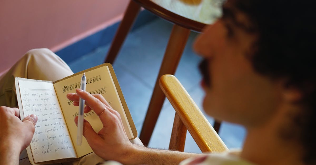 A man with a mustache writes in a notebook containing musical notations, seen from behind.