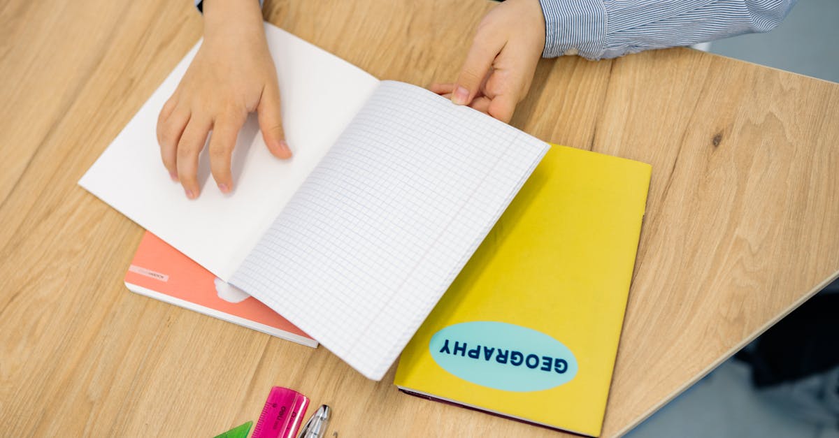 Hands flipping through a geography notebook on a wooden desk with pens and rulers.