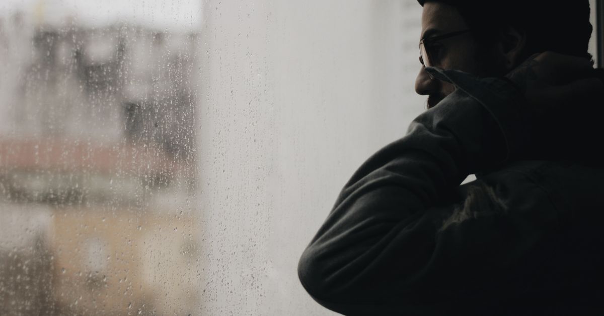 Person mit Muetze schaut an einem Regentag aus dem Fenster.