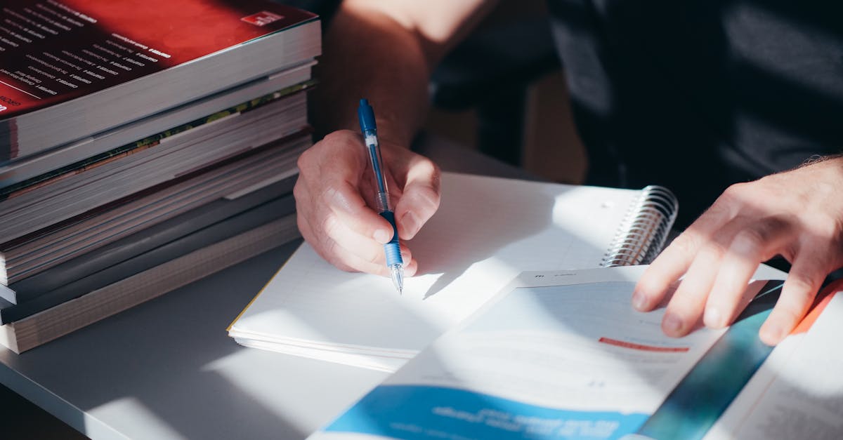 A person writing notes in a notebook with a stack of textbooks nearby, captured indoors.