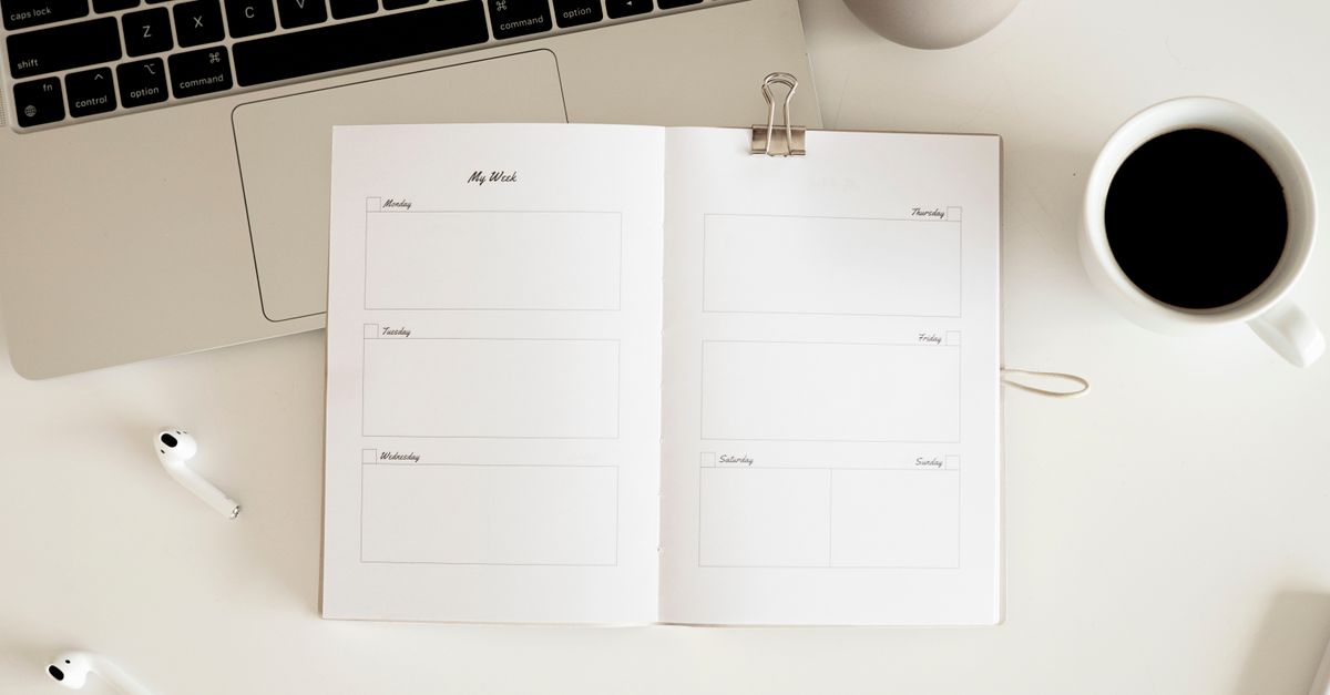 Overhead view of a desk with planner, coffee, laptop, and earbuds in a minimalist style.