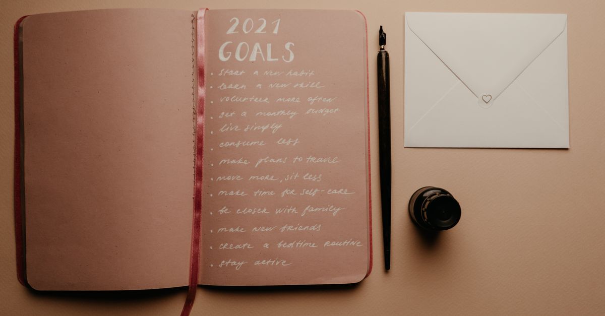 Open notebook with 2021 goals, calligraphy pen, envelope, and ink jar on neutral background.
