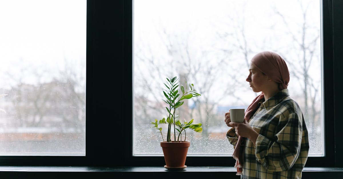 A woman with a headscarf holding a mug, looking out the window, symbolizing recovery.