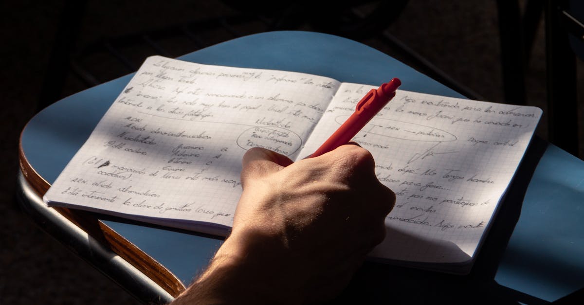 Handwriting notes with a pen on an open laptop desk in warm daylight.